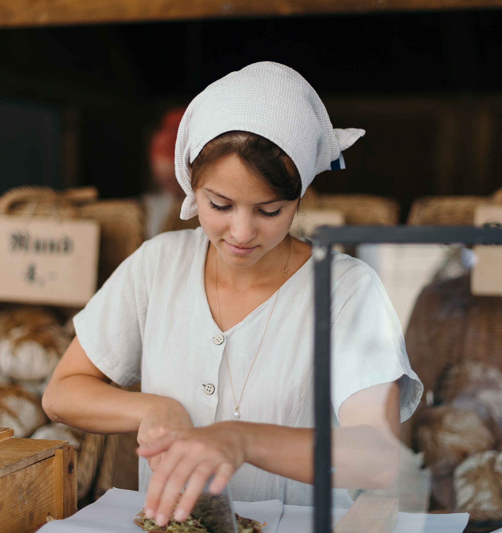 Abbildung zeigt eine junge Frau mit weissen Kopftuch und einer weissen Bluse bei der Arbeit am Küchentisch